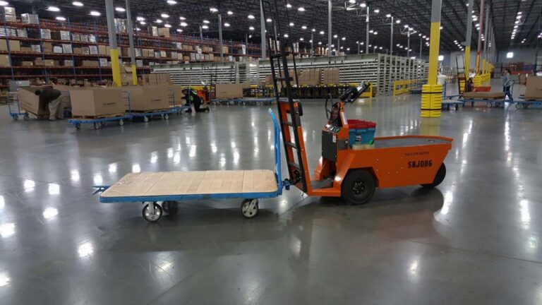 An electric tugger towing a warehouse cart, showcasing the superior alternative to forklifts for material handling.